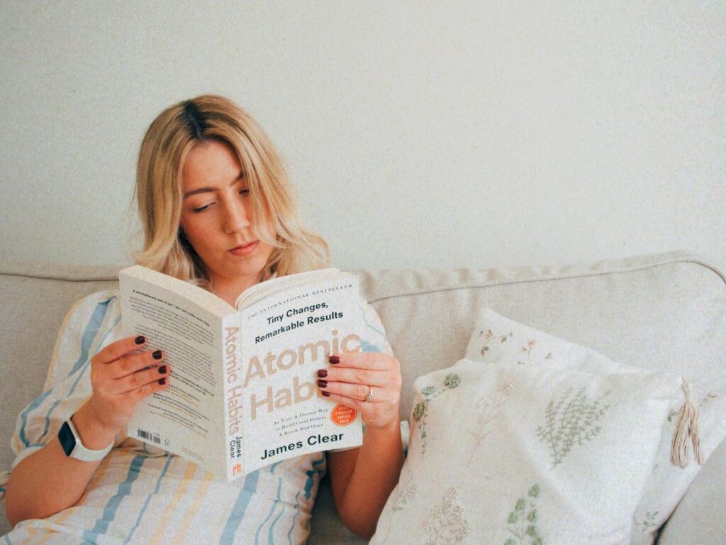 A photo of Lucie reading Atomic Habits on the sofa, ahead of giving an Atomic Habits review