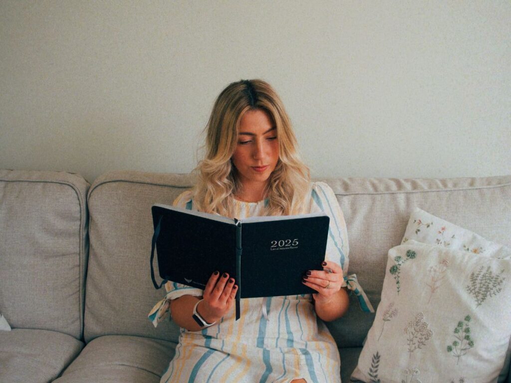 A photo of Lucie reading her Law of Attraction Planner by Freedom Mastery on the sofa as she asks herself the question, "Why do I keep comparing myself to others?"