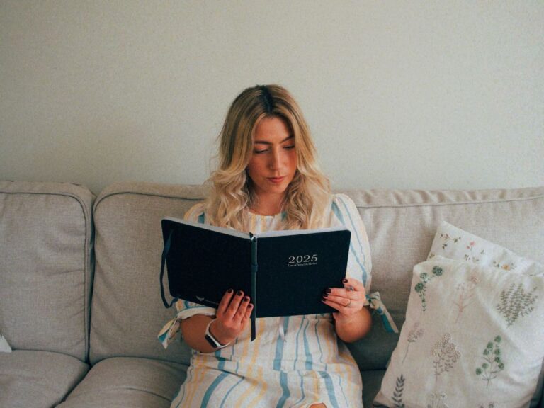 A photo of Lucie reading her Law of Attraction Planner by Freedom Mastery on the sofa as she asks herself the question, "Why do I keep comparing myself to others?"